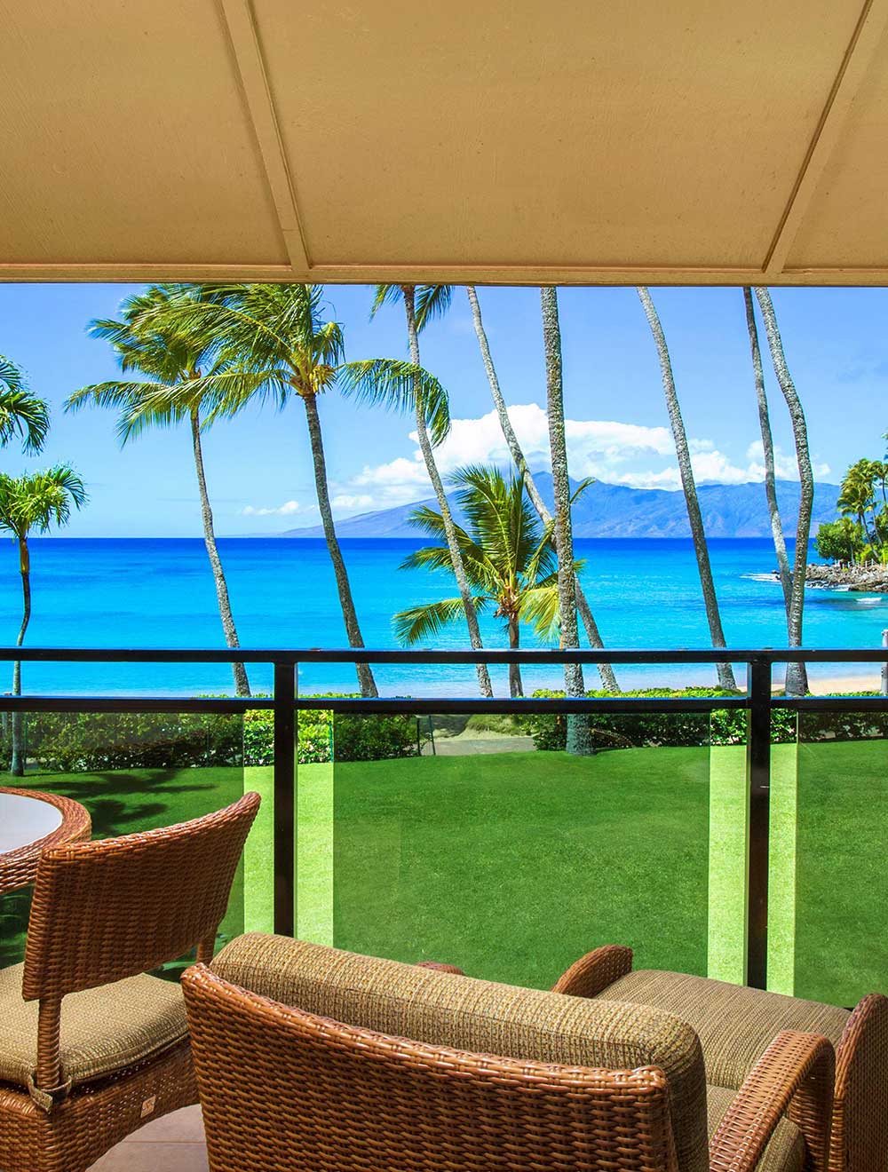 Private lanai with chairs overlooking palm trees and oceanfront lawn